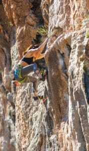 young woman climbing a steep cliff face after using the best natural energy supplements